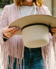 Frau in Fransenjacke hält beigen Filzhut