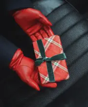 Geschenke Guide Rote Handschuhe aus Leder mit Geschenk in rot kariertem Papier mit grünen Akzenten auf einem Autositz